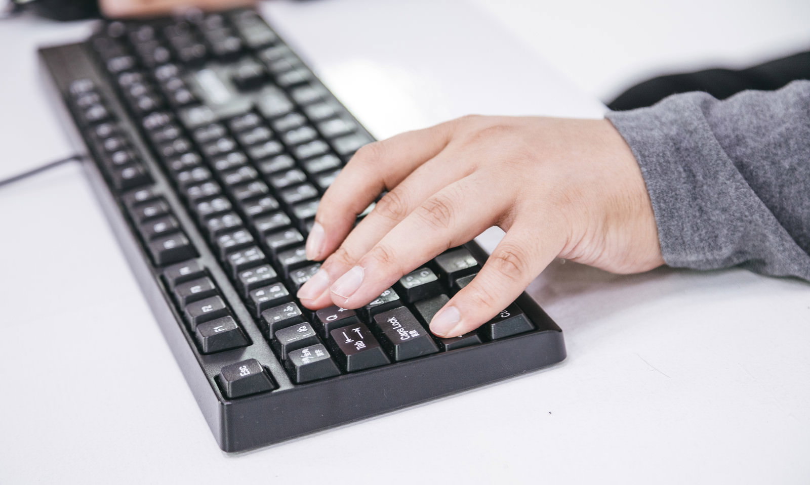 グレーのスーツを着た人がキーボードでShift+Wキーを押している手［モデル：段田隼人］