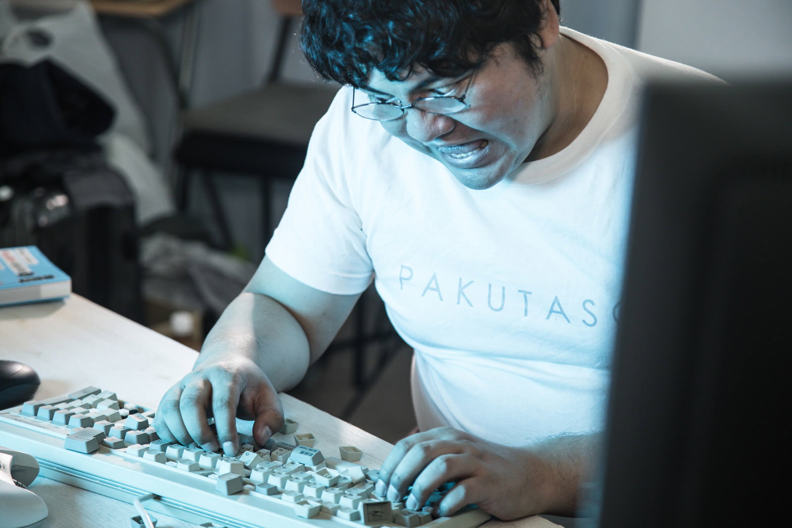 白いTシャツの男性がデスクでキーボードを激しく叩いている様子［モデル：段田隼人］