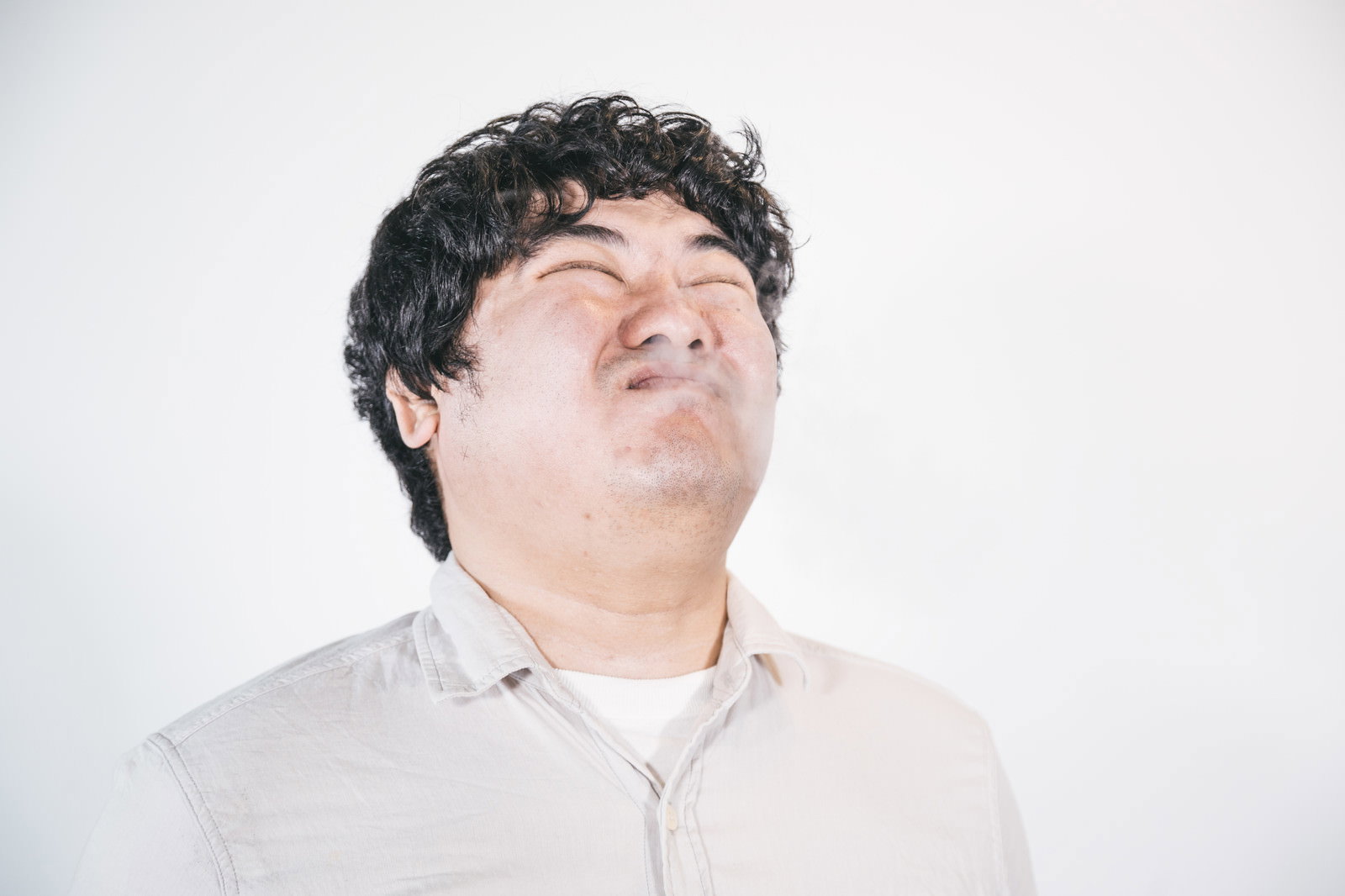白いシャツの男性が煙を嫌がって顔をそむけている様子［モデル：段田隼人］