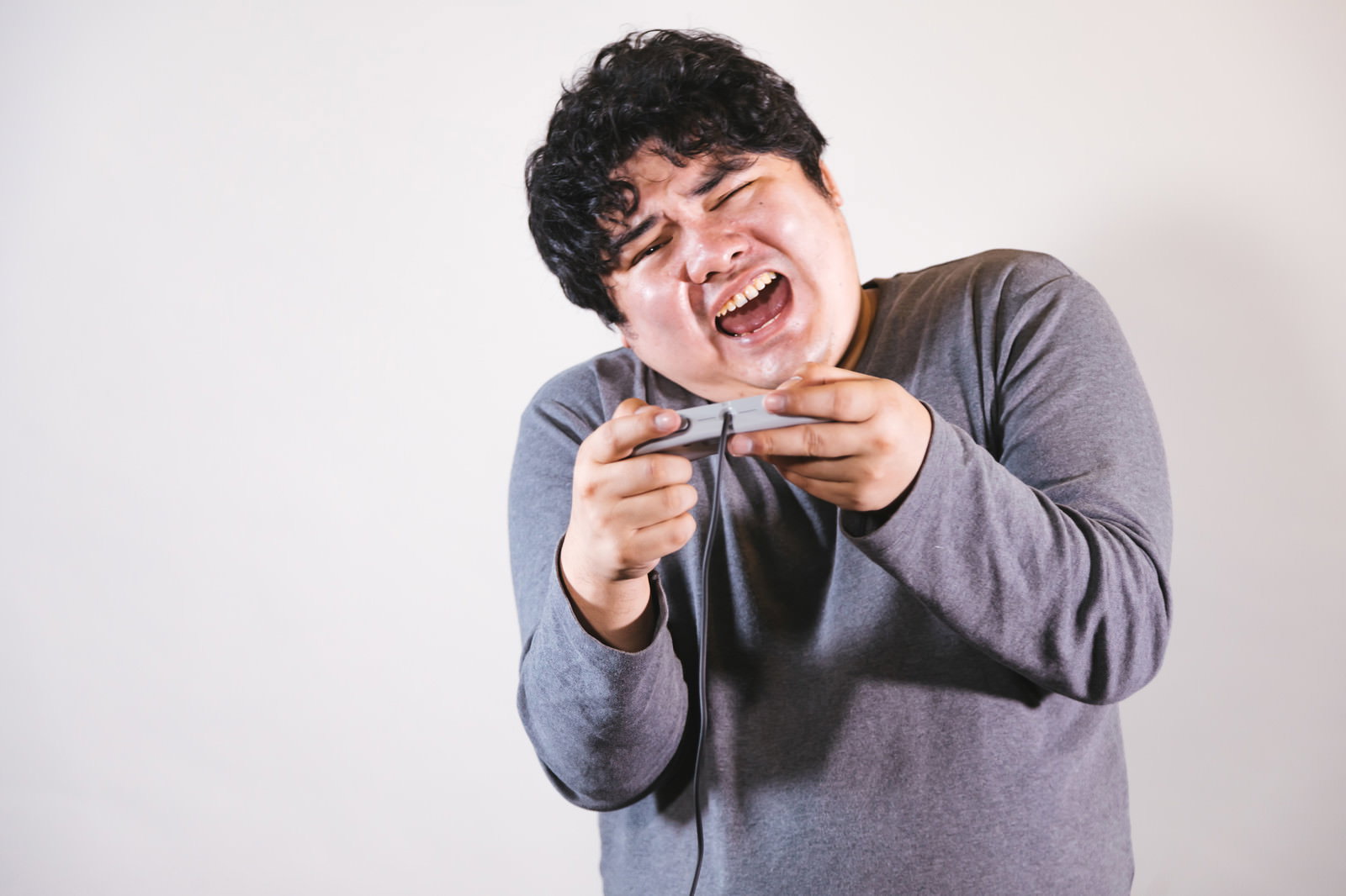 グレーのパーカーを着た男性がゲームコントローラーを持って叫んでいる［モデル：段田隼人］