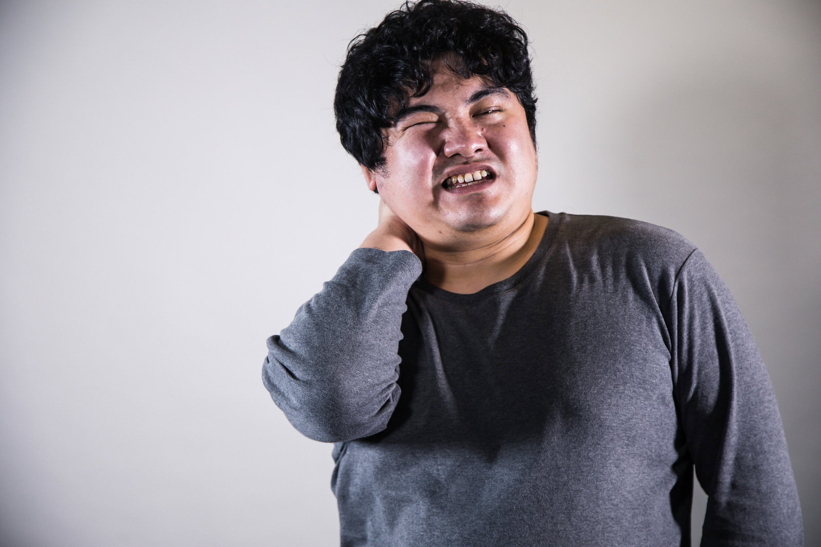 首の後ろをつかんで痛がる男性［モデル：段田隼人］