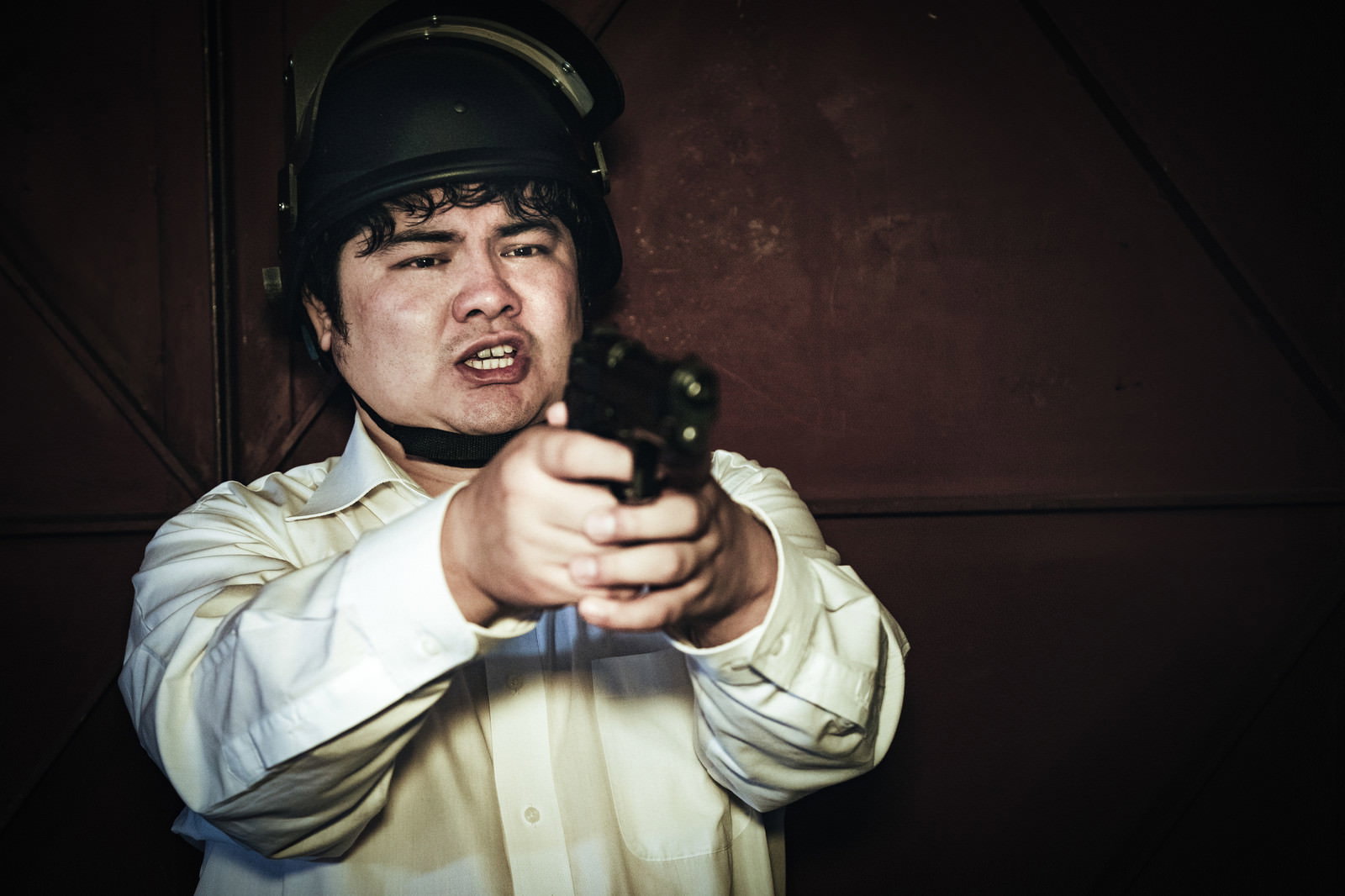 両手で拳銃を構えて狙いを定める男性［モデル：段田隼人］