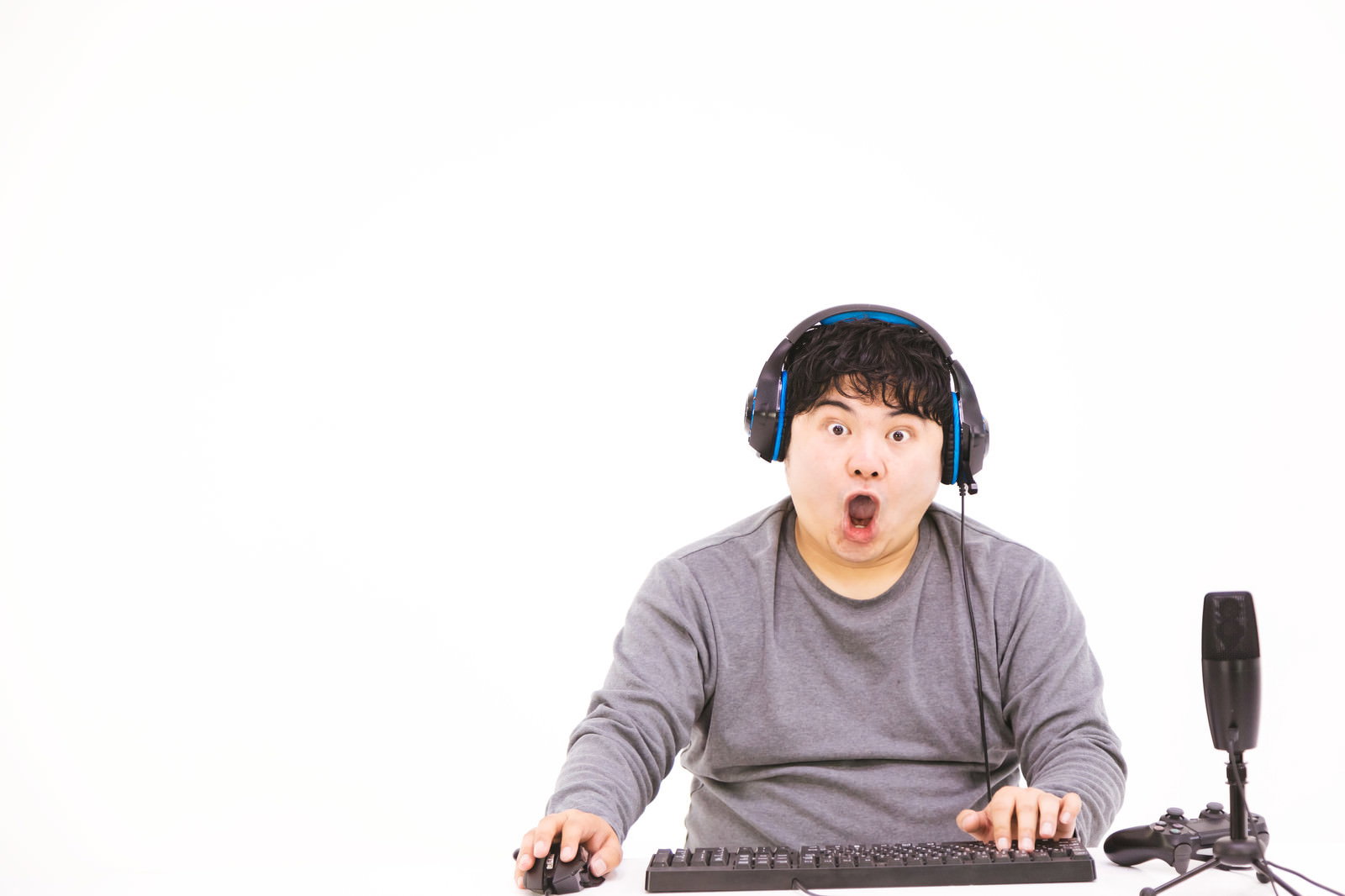 ヘッドフォンを装着してゲームをしながら雄叫びをあげるグレーのトレーナーの男性［モデル：段田隼人］