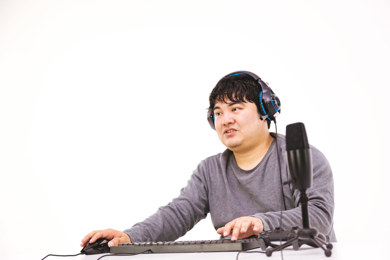 グレーシャツ姿でヘッドセットを装着し、デスクのキーボードに向かう男性配信者［モデル：段田隼人］