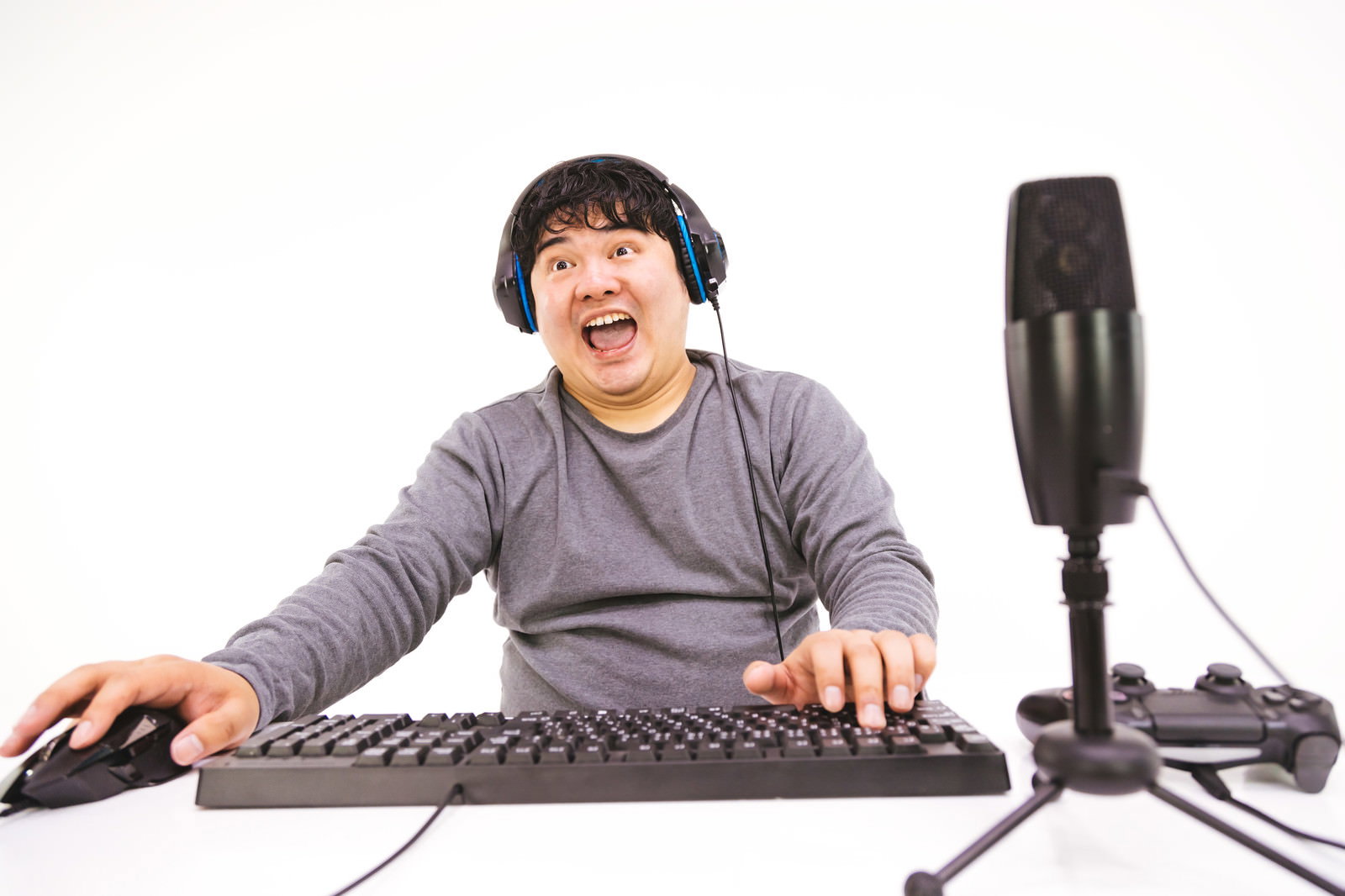 ヘッドセットを着けてマイクの前で興奮している男性ゲーマー［モデル：段田隼人］