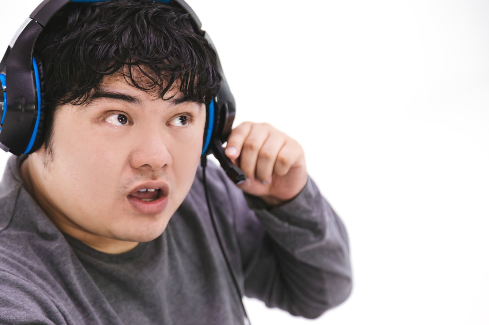 ヘッドセットを着けたグレーパーカーの男性が驚いた表情で右手を上げている［モデル：段田隼人］