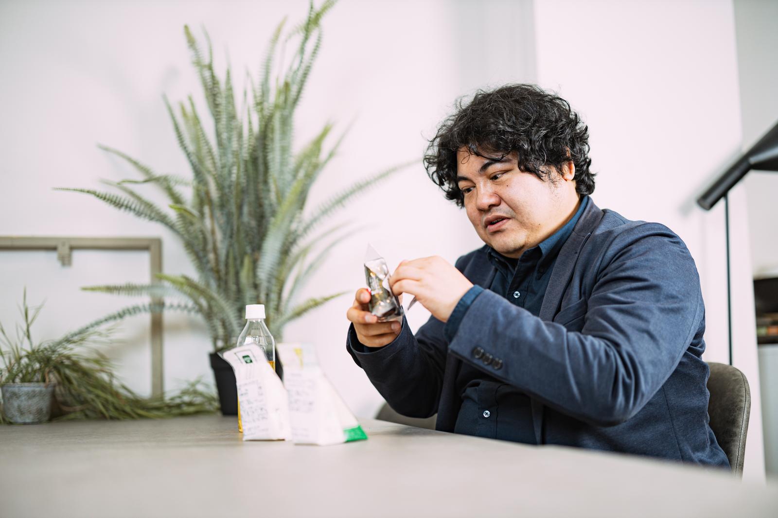 オフィスのデスクで弁当を見つめる紺色シャツの男性［モデル：段田隼人］