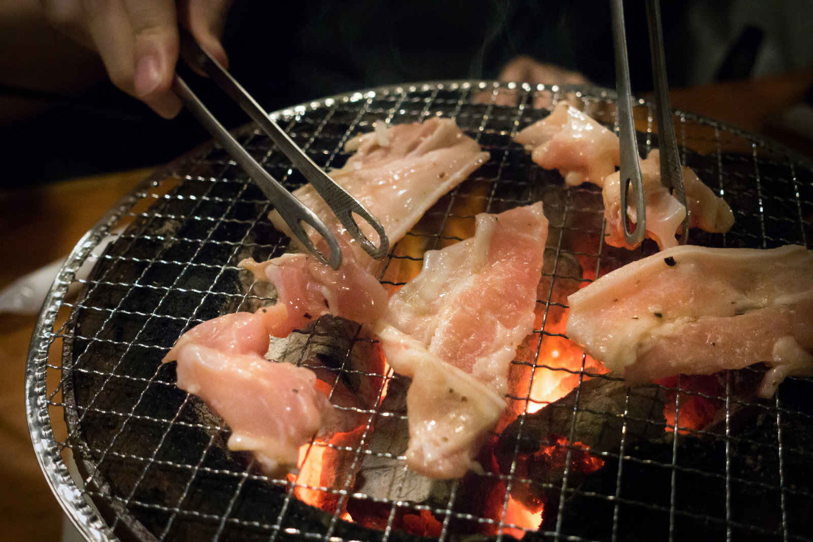 炭火の網で焼かれている豚肉から湯気が立ち上がっている様子