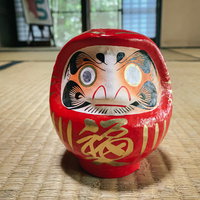 和室の畳に置かれた片目のままの赤い達磨さんの祈願置物の写真