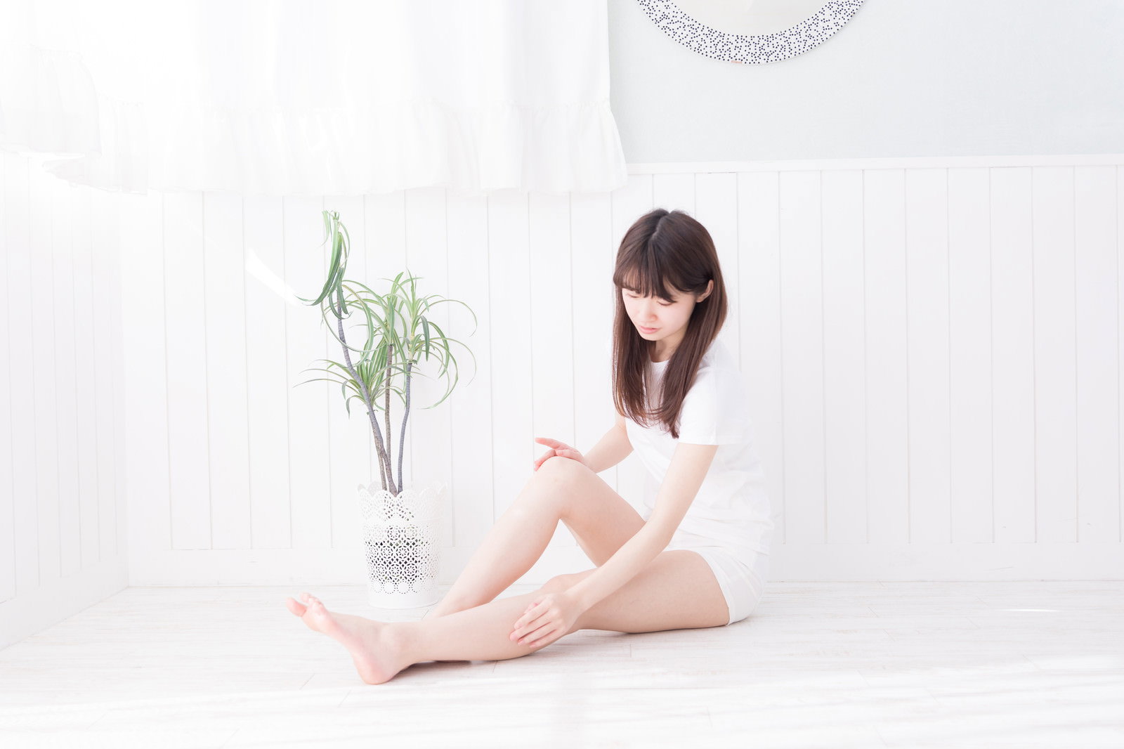 白いトップを着て座り、脚をケアする女性の脱毛肌［モデル：川子芹菜］