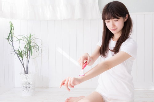 白い服姿で左腕を丁寧にセルフ脱毛する女性