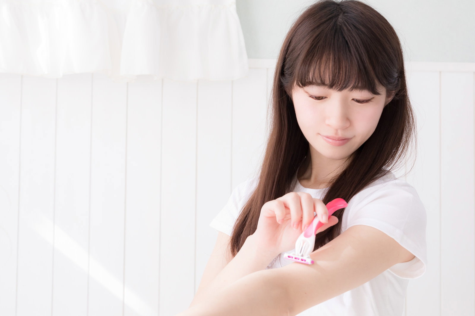 白いタオルを身に着けた女性が左腕をカミソリで剃毛している［モデル：川子芹菜］