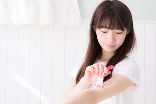 白いタオル姿で左腕をカミソリで慎重に剃毛する女性