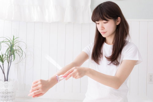 右腕にカミソリをあてて腕の毛を剃り始める女性