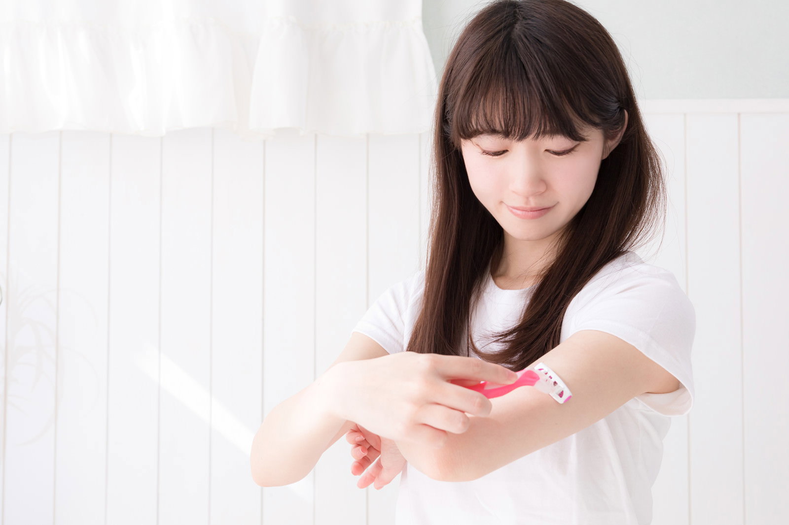 白い服を着た女性がカミソリで腕のムダ毛を処理している様子［モデル：川子芹菜］