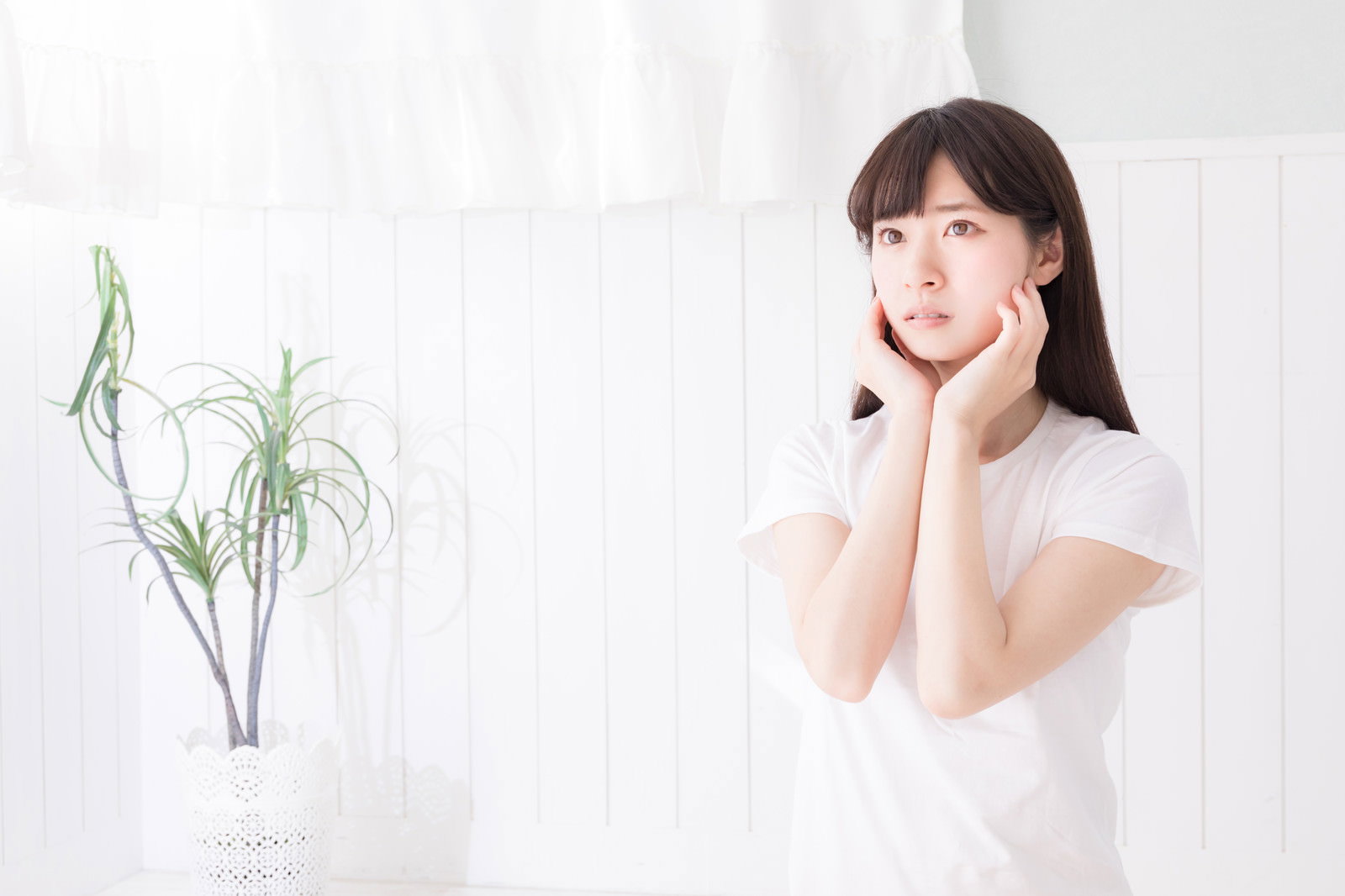 白いトップスを着て頬に手を当てるポーズの女性［モデル：川子芹菜］