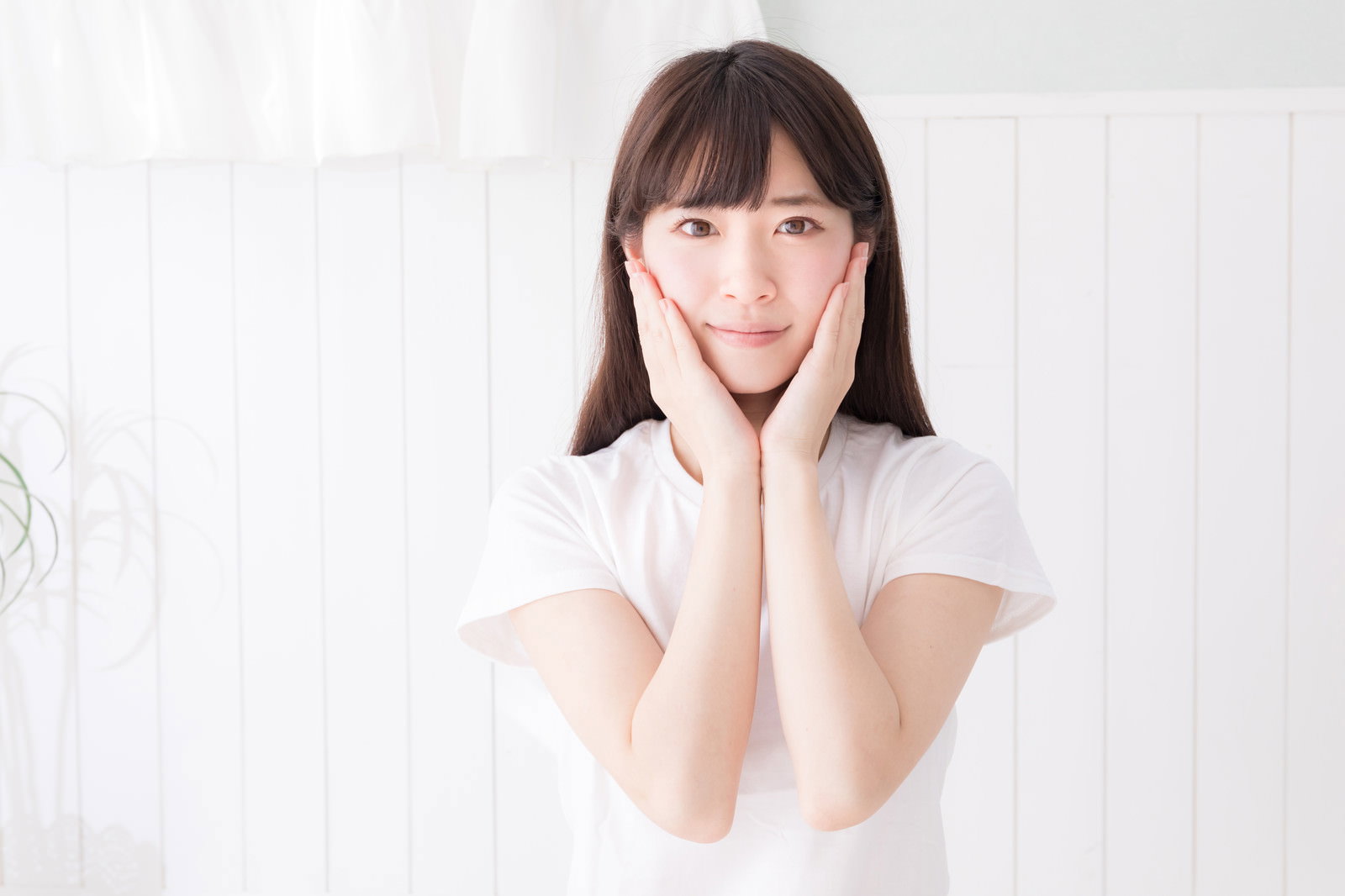 白い服を着た女性が両手のひらを頬に当てている美容イメージ［モデル：川子芹菜］