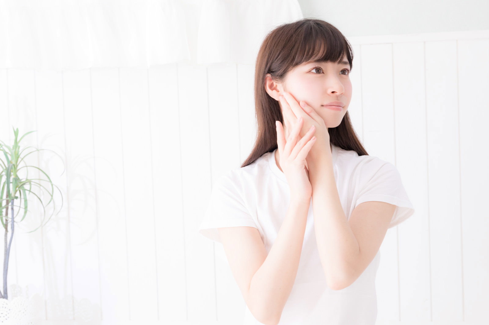 顔に手を添え遠くを見つめる白いトップスの女性［モデル：川子芹菜］