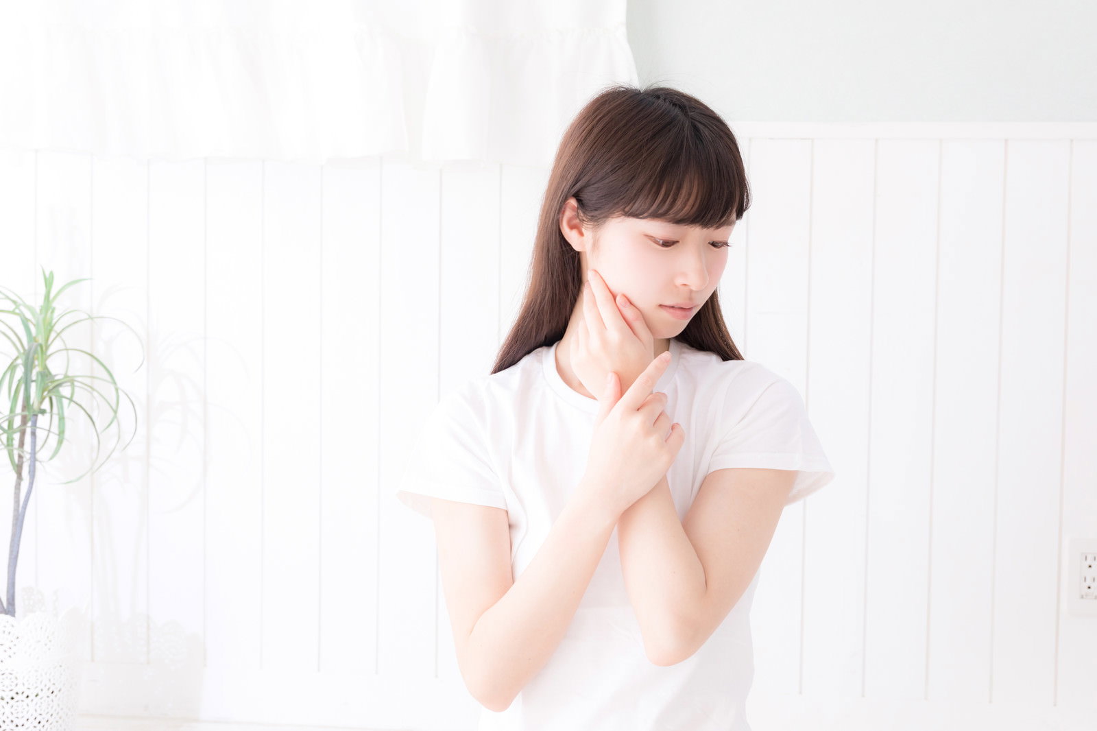 白い服を着た女性が首元に手を添えて俯いている様子［モデル：川子芹菜］