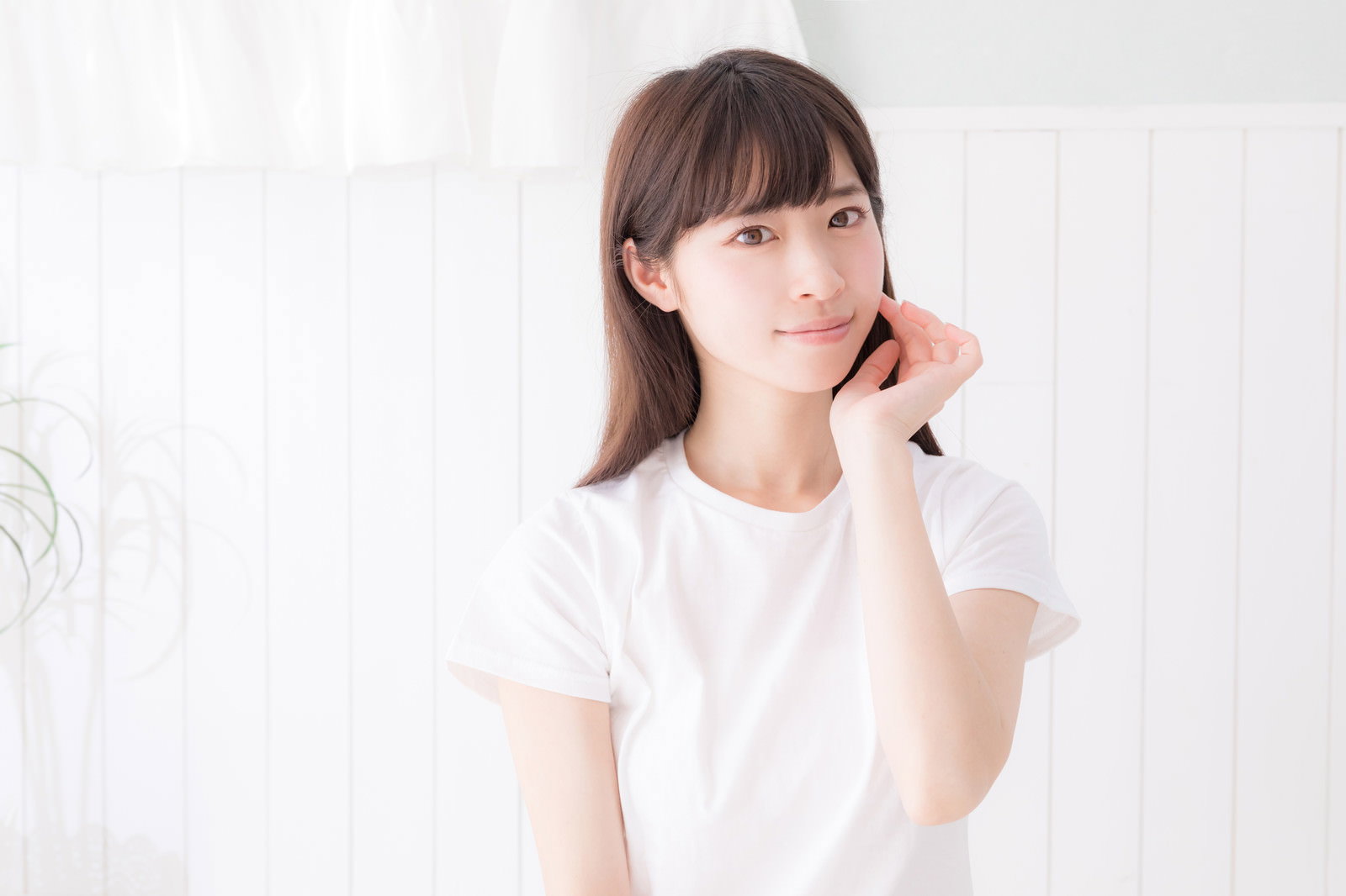 白い服を着た美白の女性が片手を顔に添えてカメラ目線でポーズを取っている［モデル：川子芹菜］