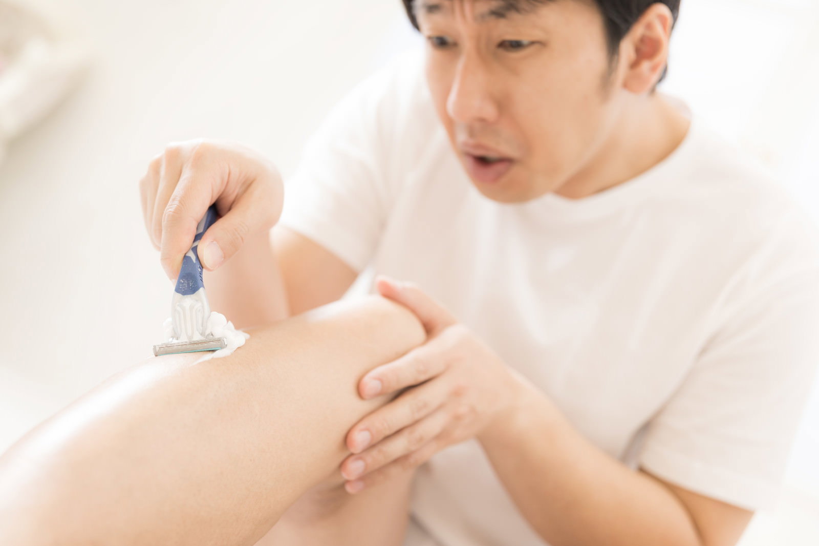 白いタオルを腰に巻いた男性がカミソリで右足のすね毛を剃っている［モデル：大川竜弥］