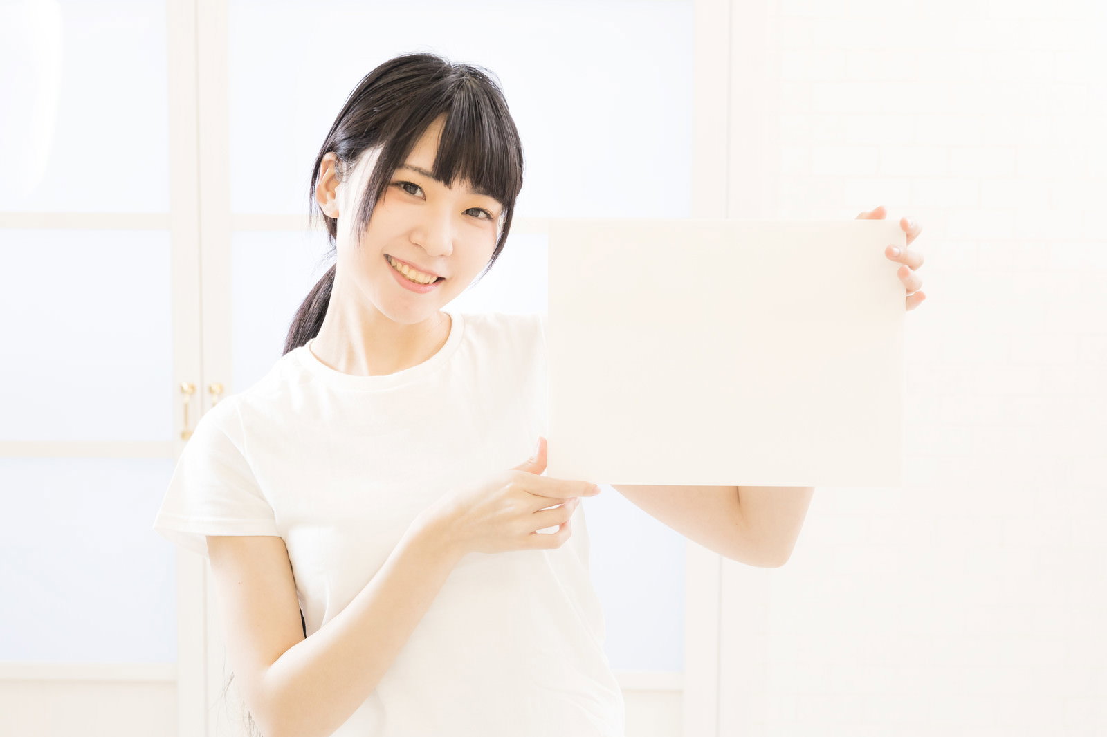 白いパネルを両手で持ちながら笑顔でポーズを取るツインテールの女性［モデル：緋真煉］