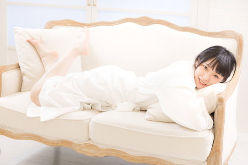 白いバスローブ姿でソファーに寝転ぶ若い女性