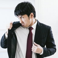 自分の脇のにおいに顔を歪める黒スーツの男性の写真