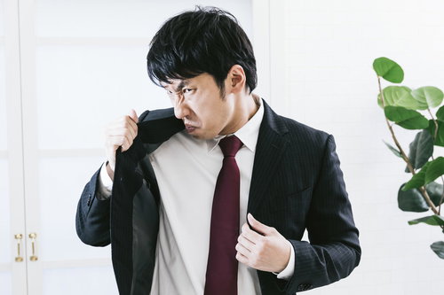 自分の脇のにおいに顔を歪める黒スーツの男性