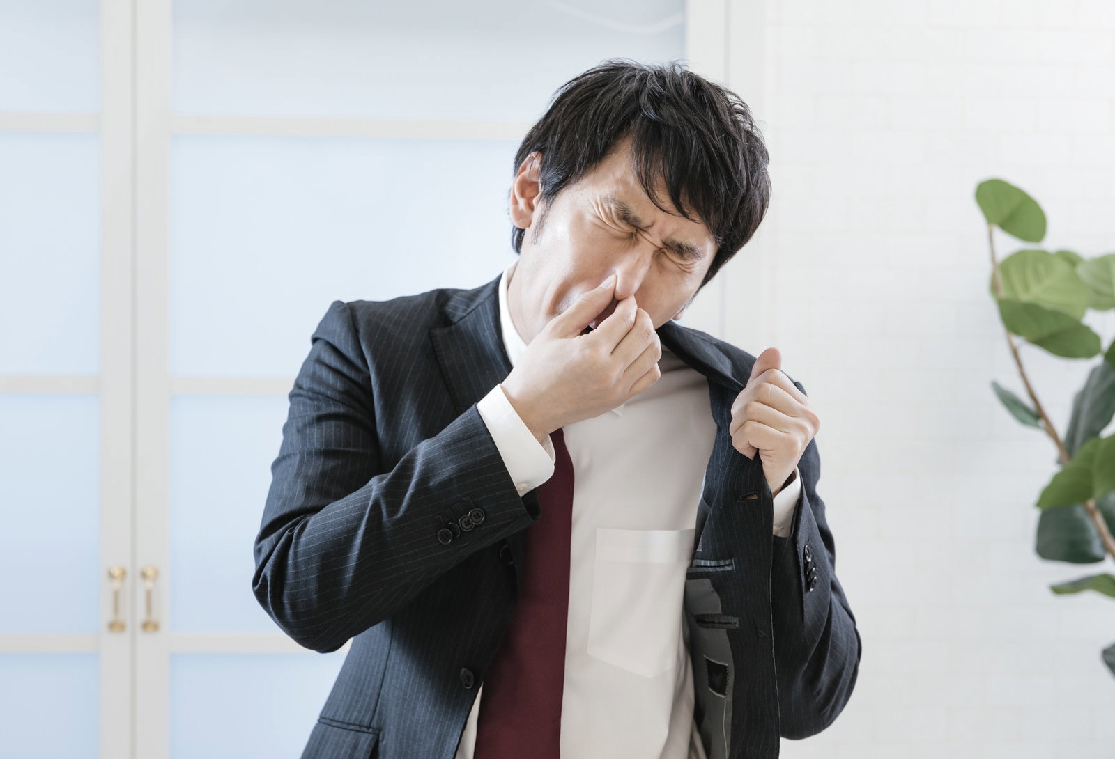 体臭を気にして鼻に手を当てて困った表情を見せるスーツ姿の男性［モデル：大川竜弥］