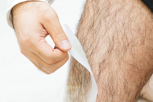 剛毛なすね毛に貼った脱毛シートを剥がす男性