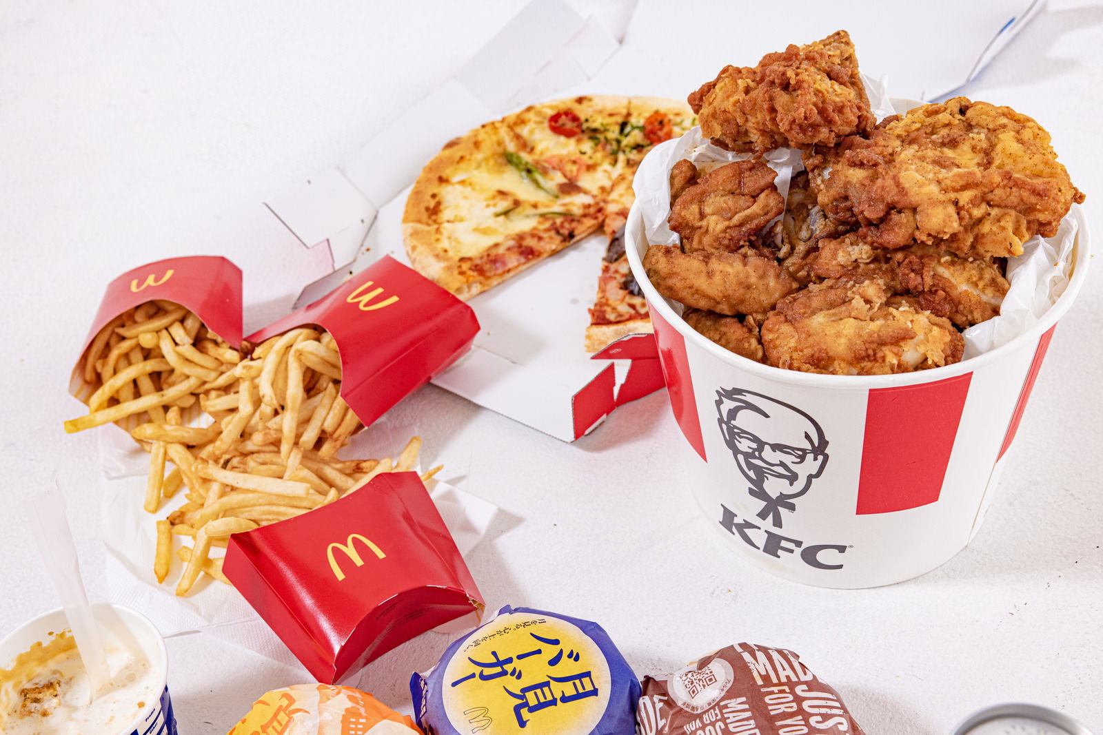 ケンタッキーのチキンとポテト、ピザが白いテーブルに並んでいる