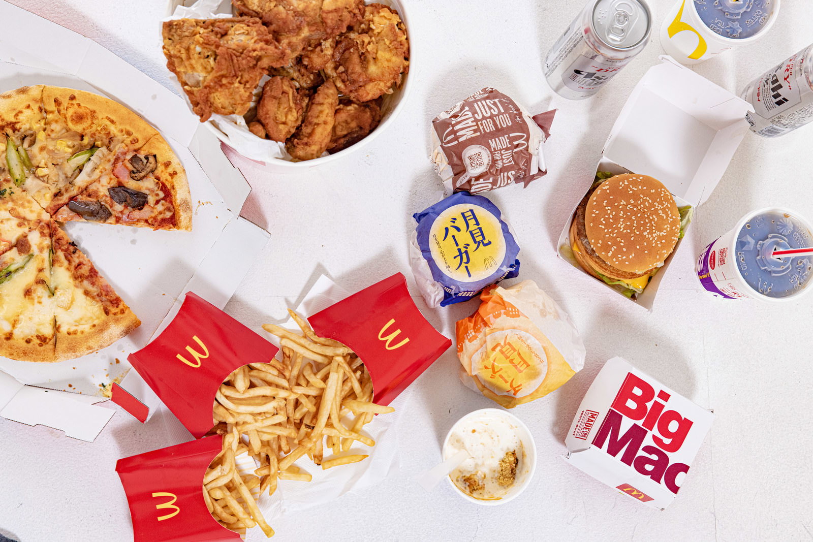ピザ、フライドチキン、ハンバーガー、フライドポテトなどのファーストフードが白い背景に並んでいる