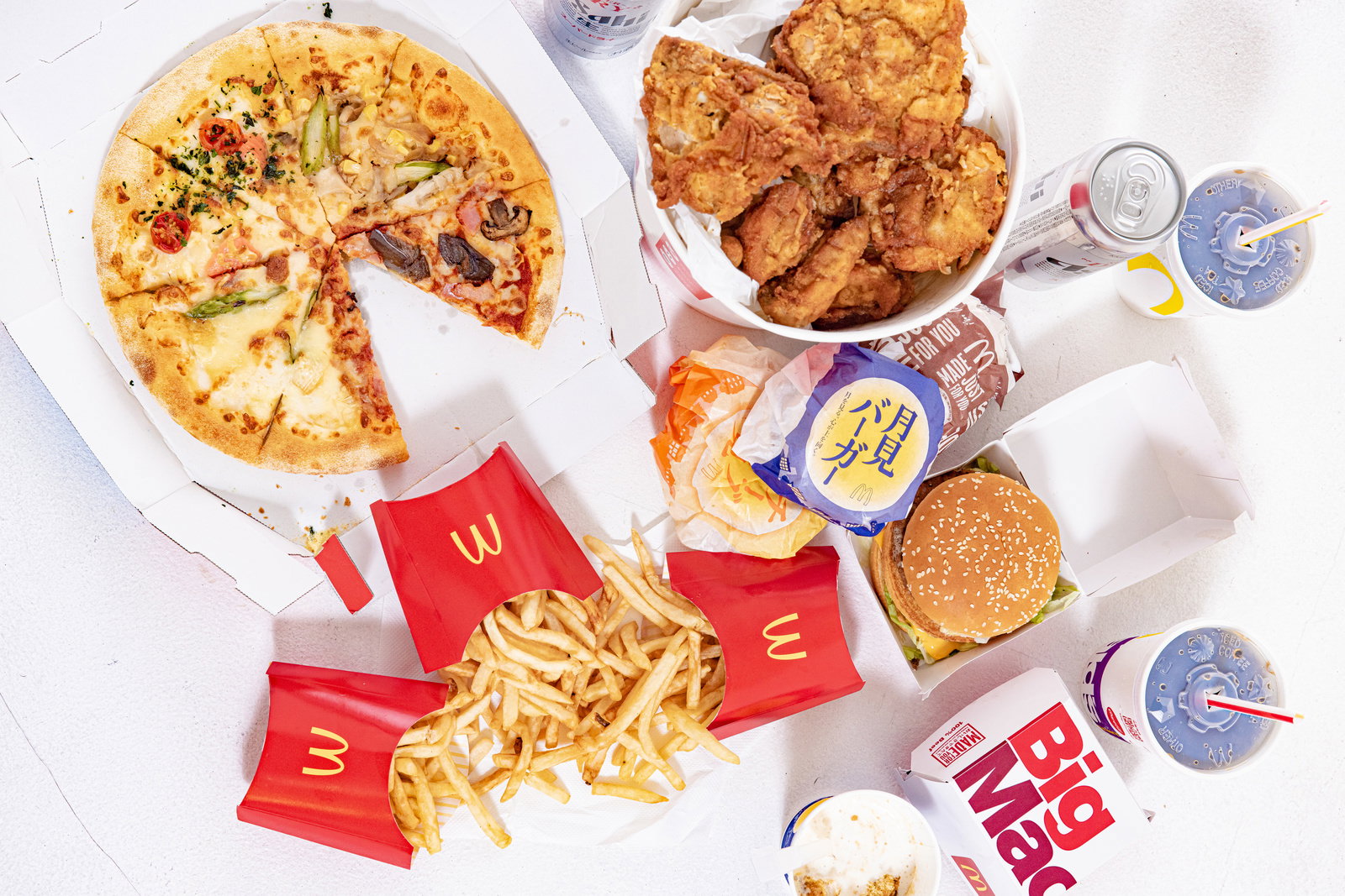 ピザ、フライドチキン、ハンバーガーなどの高カロリー食が白い容器に盛り付けられている