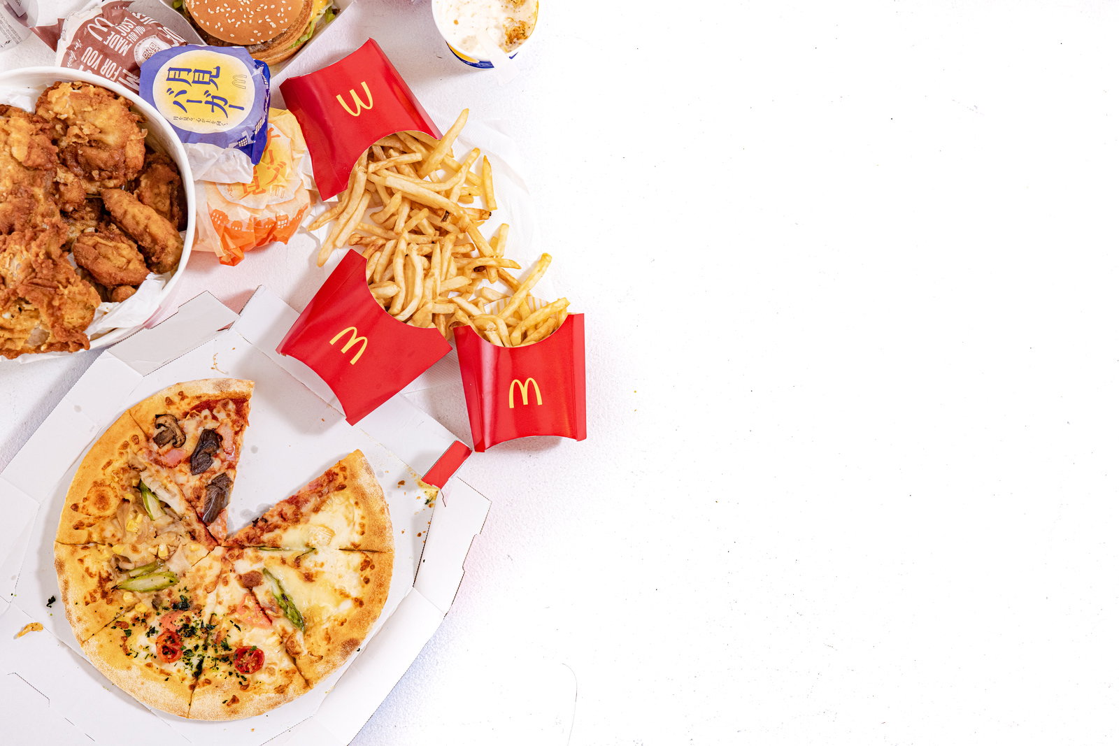 テーブルの上に並ぶフライドチキン、ピザ、フライドポテト、ハンバーガーなどのジャンクフード