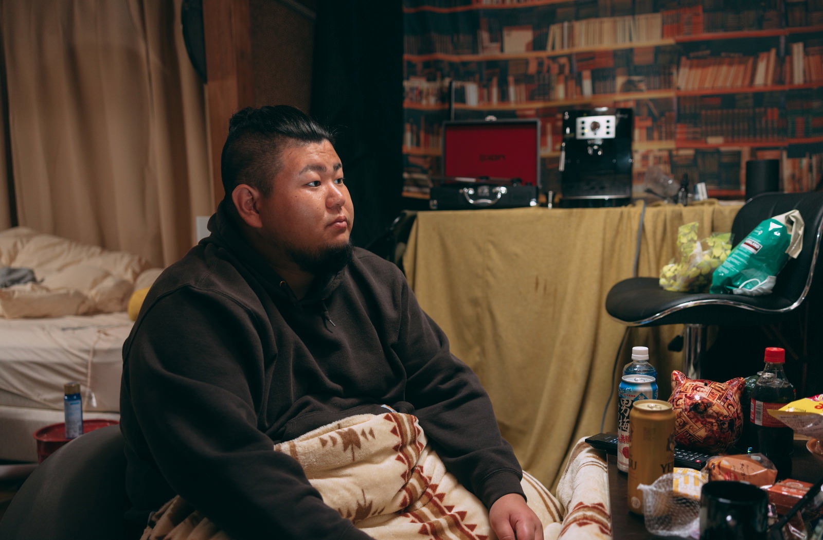 黒いパーカーを着た無精髭の男性がソファーに座ってテレビを見ている［モデル：ダルマ親方］