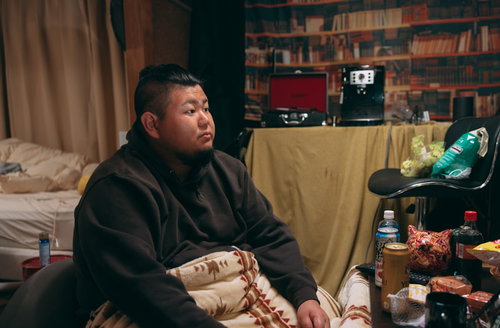 汚部屋でテレビを見る無精髭の太った男性のライフスタイル