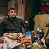 片づけられない机の上でリモコンを手にするぐうたらな男性の写真