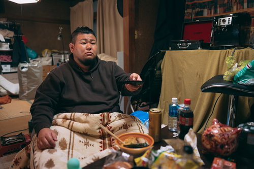 片づけられない机の上でリモコンを手にするぐうたらな男性