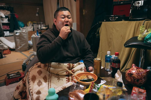 汚部屋でマイクを握る太った男性の暴飲暴食な生活