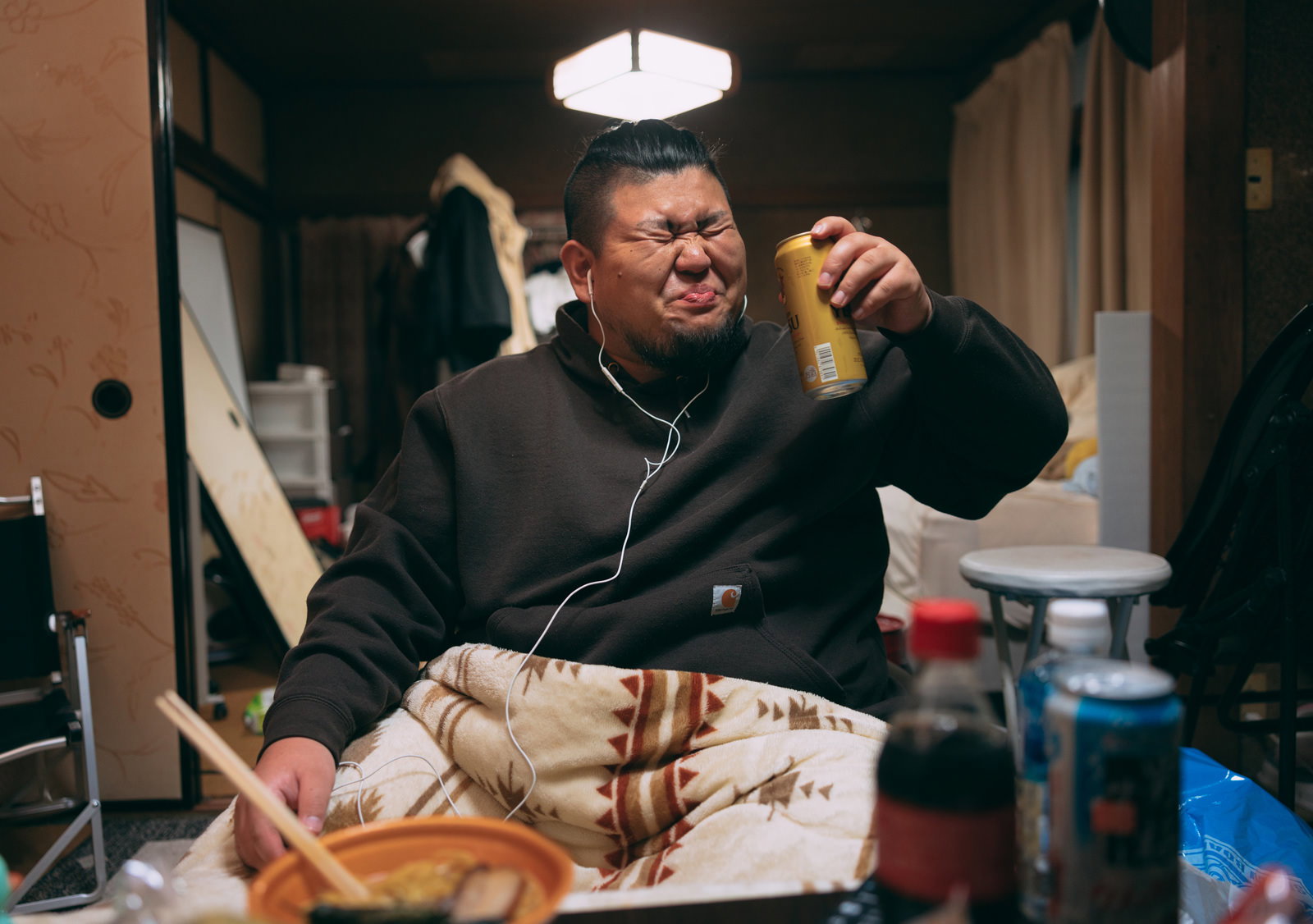 黒いスウェットの男性がイヤホンをつけて缶ビールを飲んでいる様子［モデル：ノリックス］