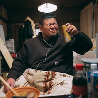 黒いスウェットでイヤホン装着しながら缶ビールを飲むぽっちゃり男性の写真