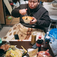 コタツに入りながらラーメンを食す無精髭の男性の写真