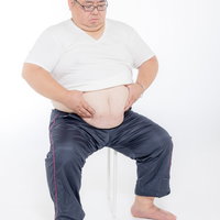 お腹の肉を寄せる膨よかな中年男性、運動不足とメタボの悩みの写真