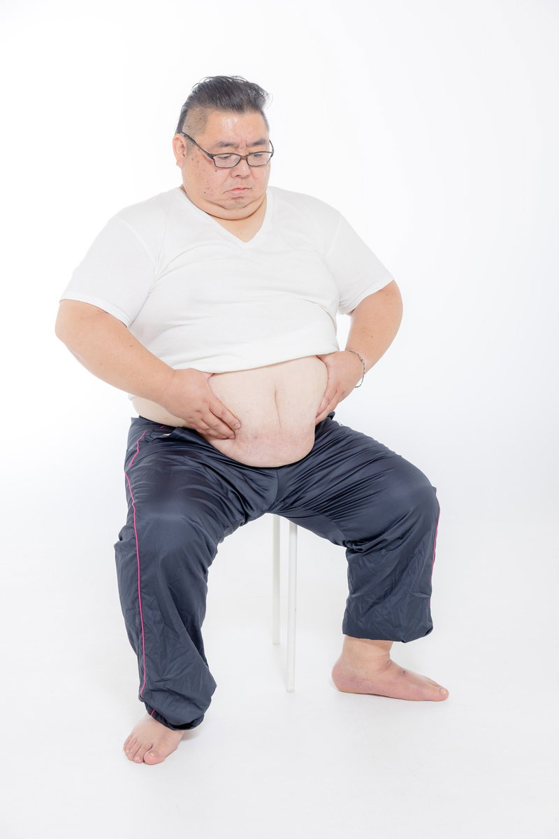 お腹の脂肪をつかむ膨よかな中年男性［モデル：ダルマ親方］