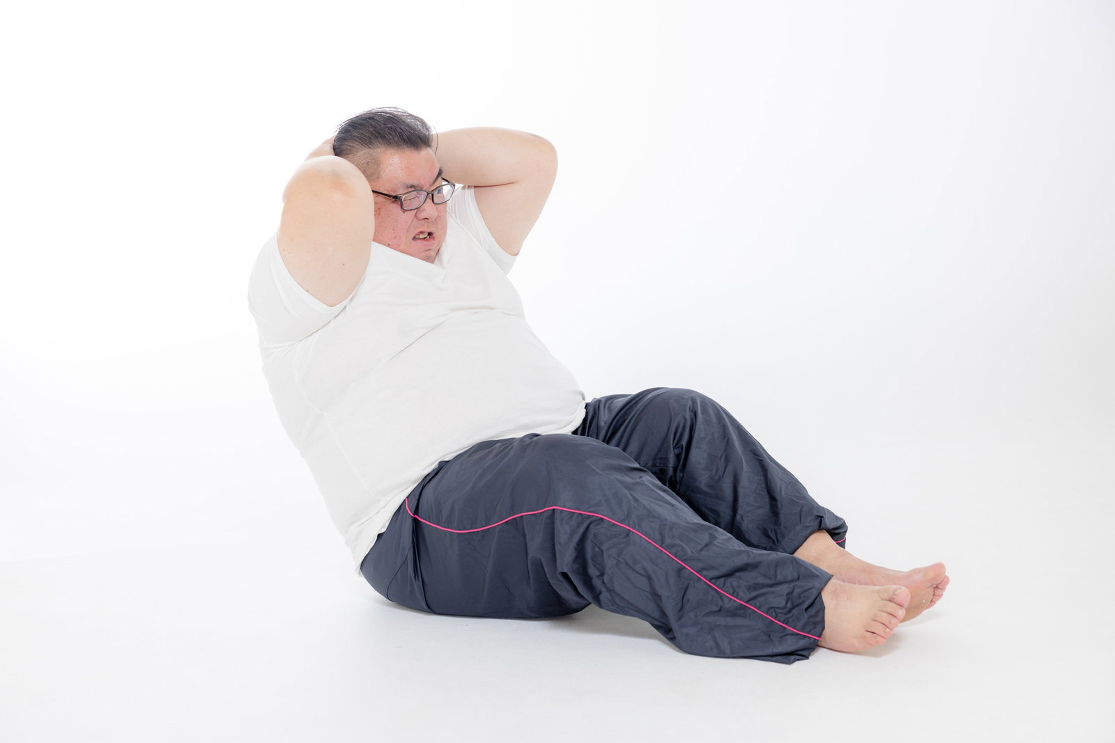 仰向けで腹筋運動をする男性が両手を頭の後ろに組んでいる［モデル：ダルマ親方］