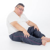 お腹の肉が邪魔でうまく座れない太った男性の写真
