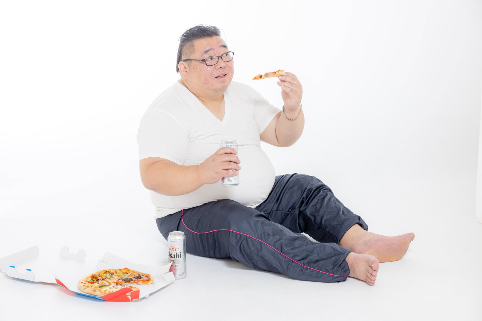 缶ビールを持ちながらピザを食べるぽっちゃり体型の男性［モデル：ダルマ親方］