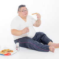 缶ビール片手にピザを食べる男性の食生活と健康管理の写真