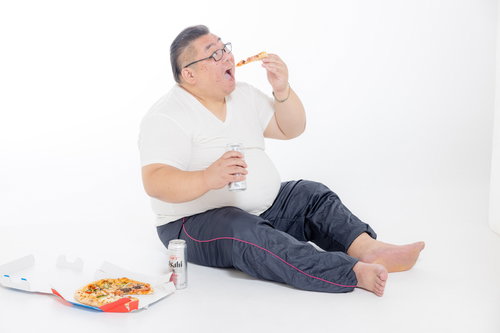 ビールを片手にピザを食べる膨よかな男性、肥満と飲酒